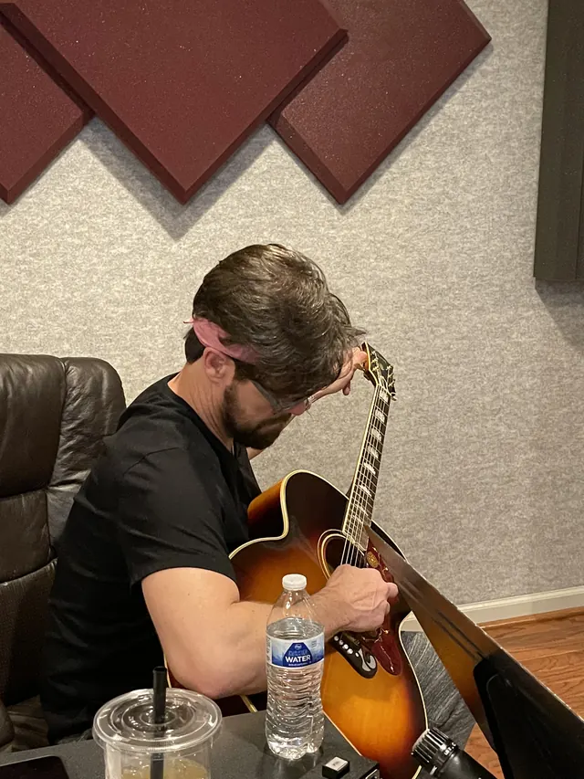 Guitarist playing a sunburst acoustic guitar in the control room