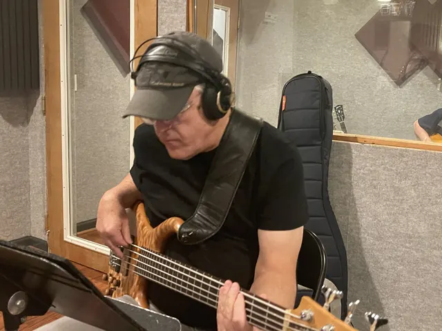 Bass player in a cap and headphones tracking by the booth door