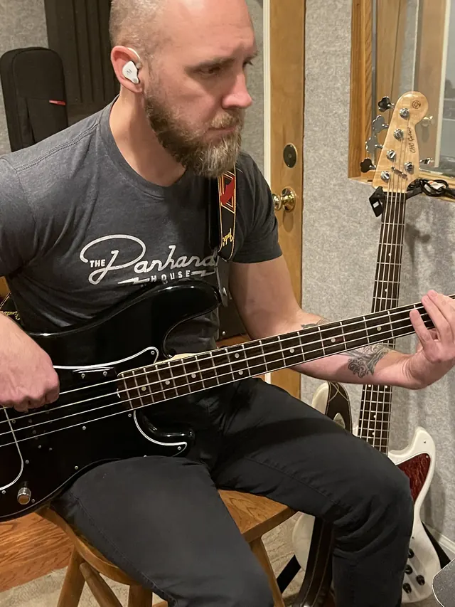 Bass player tracking on a black bass guitar in the live room