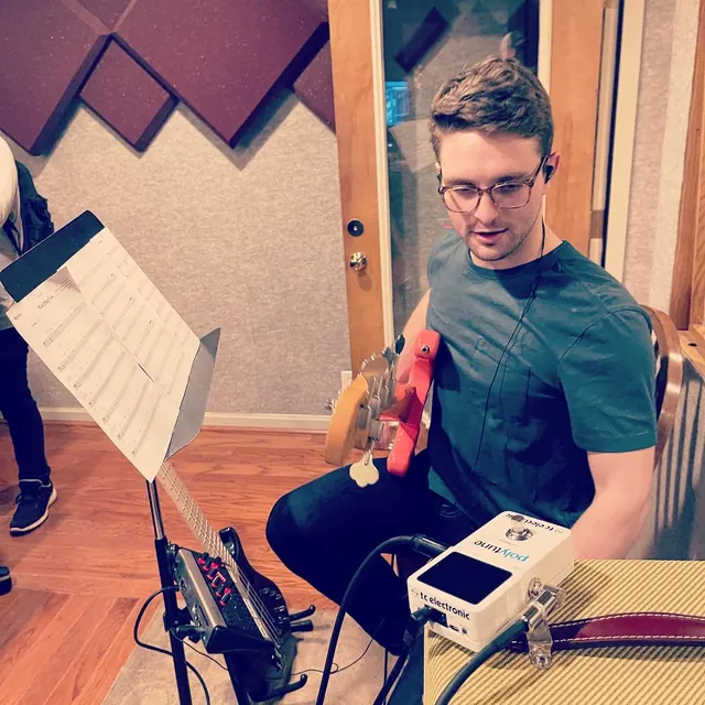 Bass player reading a chart beside his tuner pedal in the live room