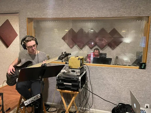 Bass player tracking in headphones beside the control room window
