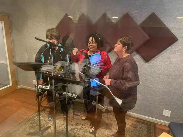 Three background vocalists singing at microphones with music stands