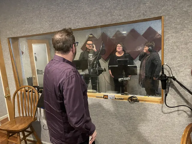 Producer in the control room watching three singers through the booth glass