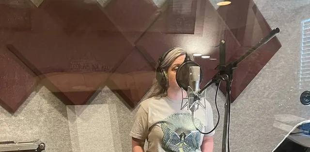 Female vocalist singing at the microphone in the vocal booth, seen through the glass