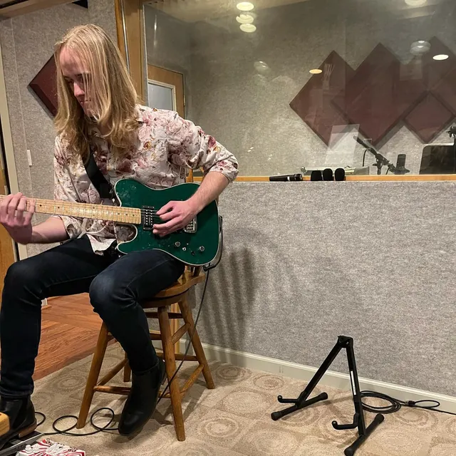Guitarist playing a green electric guitar on a stool