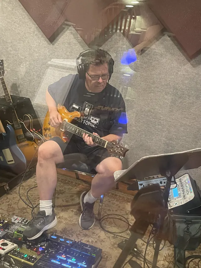 Guitarist tracking with a pedalboard, seen through the glass
