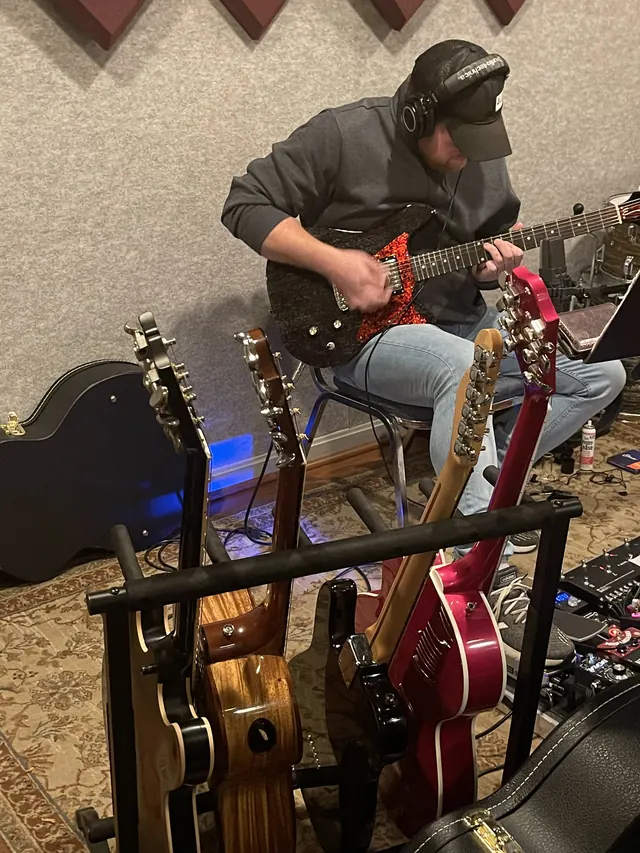 Guitarist in headphones tracking behind a rack of guitars