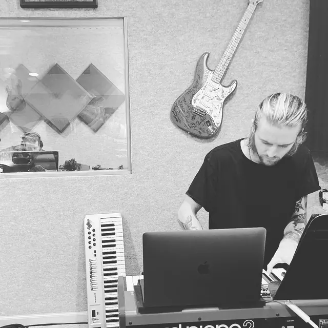 Black-and-white photo of a keyboard player working on a track at a laptop