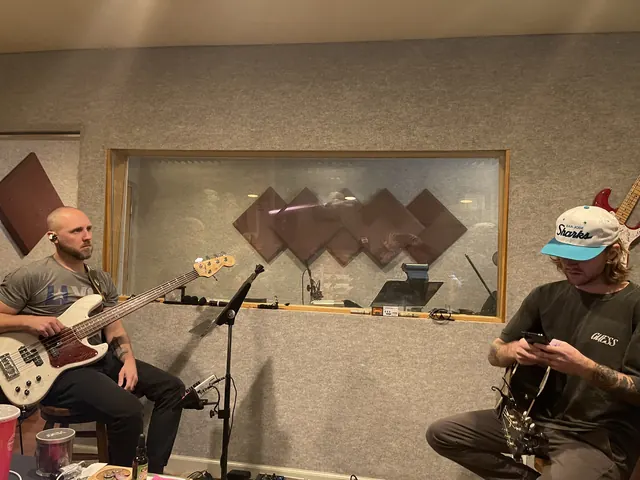 Bass player and guitarist in the live room beside the control room window