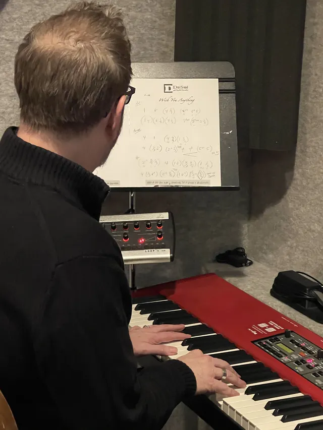 Keyboard player reading a chart at a red Nord keyboard
