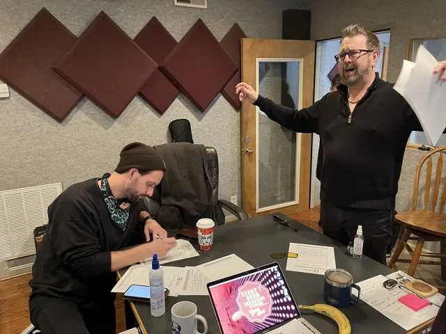Producer directing a session while a musician writes out a chart at the table