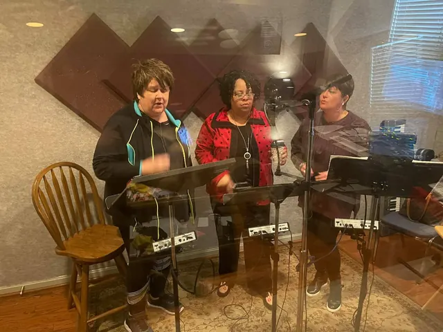 Three singers at microphones and music stands in the tracking room