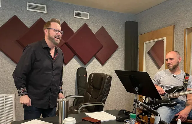 Musicians sharing a laugh during a tracking session, bass player seated with a chart