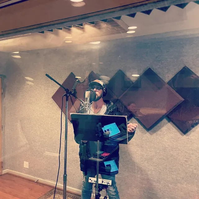 Vocalist recording in the booth, seen through the glass