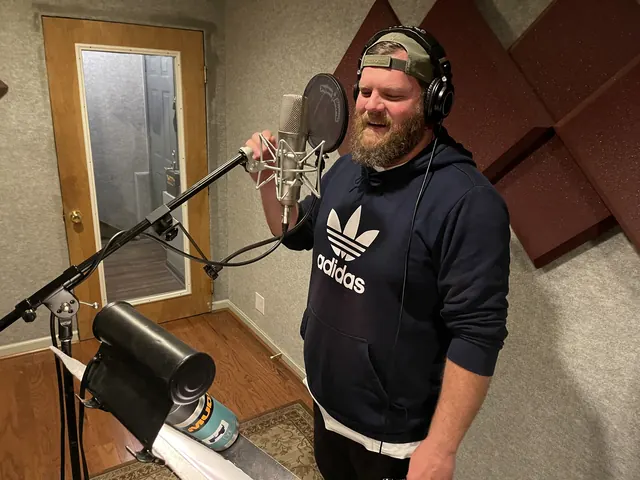 Bearded vocalist in headphones smiling at the microphone in the vocal booth
