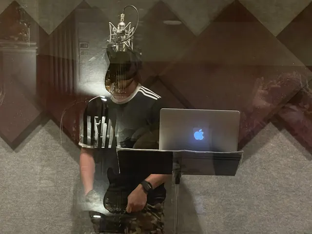 Vocalist with a laptop at the microphone, seen through the booth glass