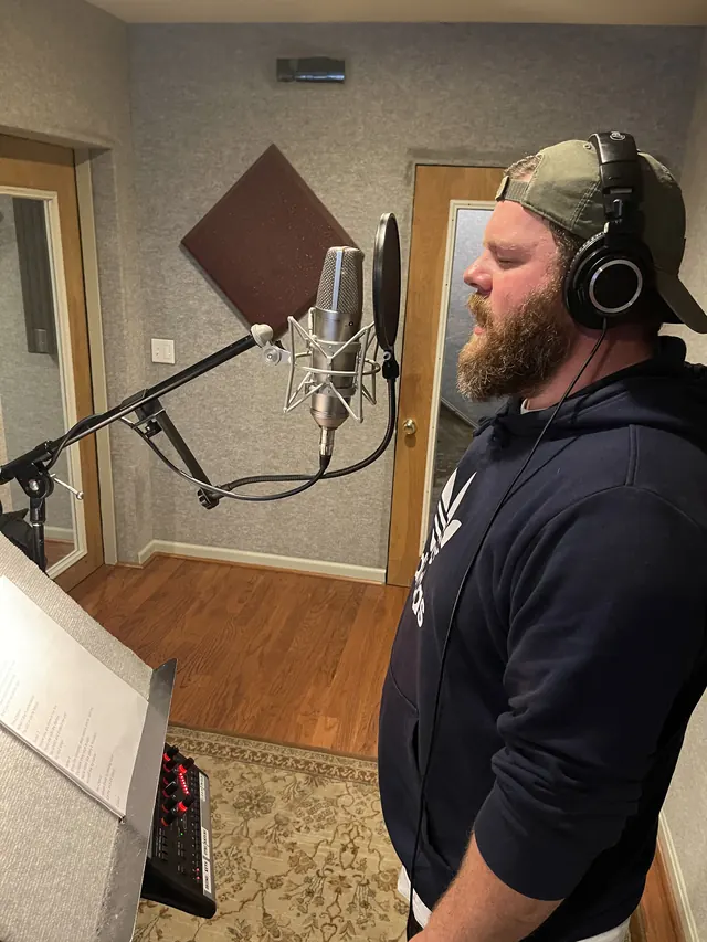Male vocalist in a ball cap singing at the microphone in the vocal booth