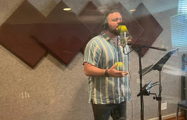Male vocalist singing into a studio microphone in the vocal booth