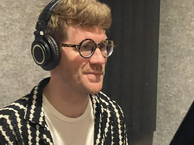 Singer in round glasses and headphones in the vocal booth